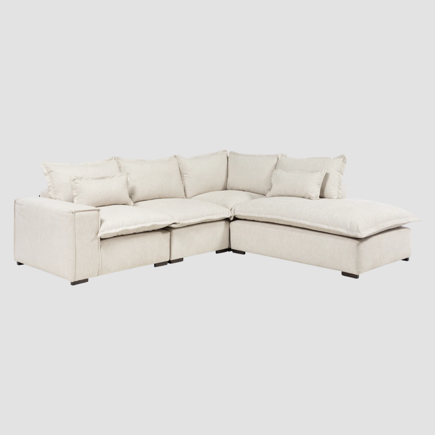 Sofá modular en color marfil con chaise a la derecha, múltiples cojines y patas oscuras que contrastan. Perfecto para tu sala.