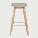 Vista frontal del banco alto Perique en color beige, con un asiento ergonómico de perfil bajo y bordes redondeados, montado sobre una estructura de cuatro patas de madera clara con un reposapiés metálico negro.