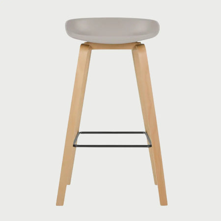 Vista frontal del banco alto Perique en color beige, con un asiento ergonómico de perfil bajo y bordes redondeados, montado sobre una estructura de cuatro patas de madera clara con un reposapiés metálico negro.