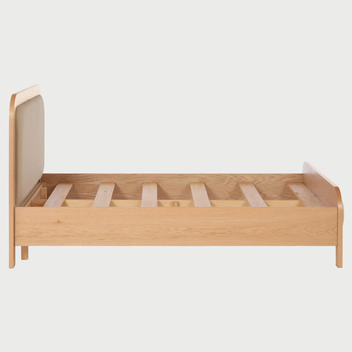 Vista lateral de la cama Iki; se aprecia el diseño de perfil bajo con largueros de madera natural y la continuidad de las líneas redondeadas que conectan la cabecera con la base, manteniendo una estética minimalista.