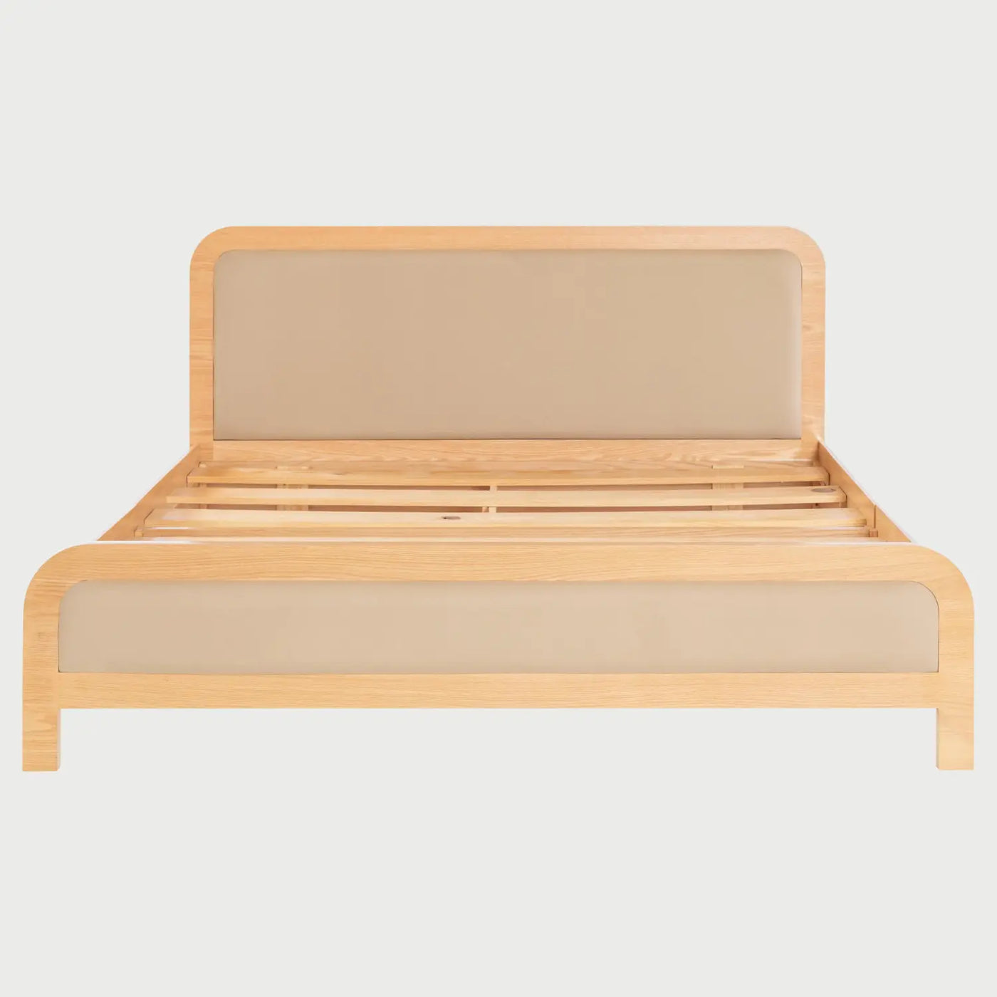 Vista frontal de la cama King Size Iki; presenta una amplia estructura de madera clara con bordes curvos y un gran panel acolchado en color beige integrado en la cabecera, complementado por un pie de cama bajo con el mismo acabado tapizado.