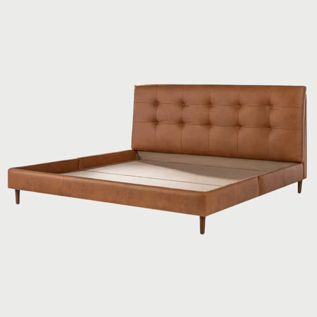 Vista en perspectiva de la cama King Size Landero; muestra la amplia cabecera acolchada con tapizado en piel sintética color café y su elegante diseño de capitonado de puntos, extendiéndose hacia una base de perfil bajo con patas de madera.