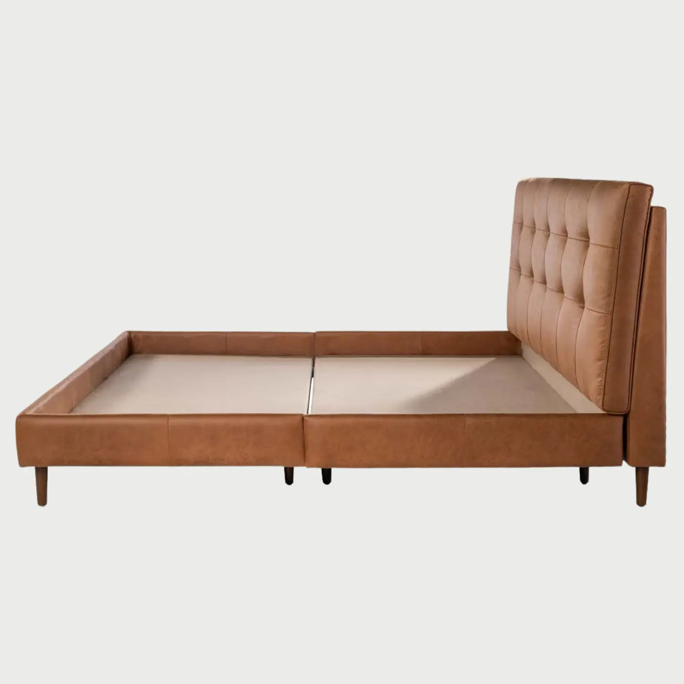 Vista lateral de la cama Landero; se aprecia el grosor del marco perimetral tapizado y la inclinación del respaldo acolchado, soportado por patas cilíndricas de madera que elevan sutilmente la estructura del suelo.