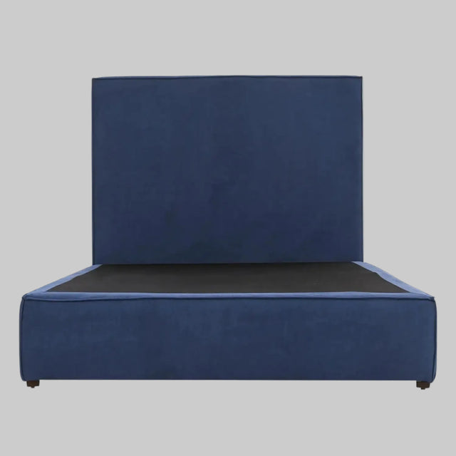 Vista frontal de la cama matrimonial Raquel; presenta una imponente cabecera alta y rectangular tapizada en terciopelo azul profundo que se integra con una base de perfil bajo del mismo tono, creando una silueta moderna y sofisticada.