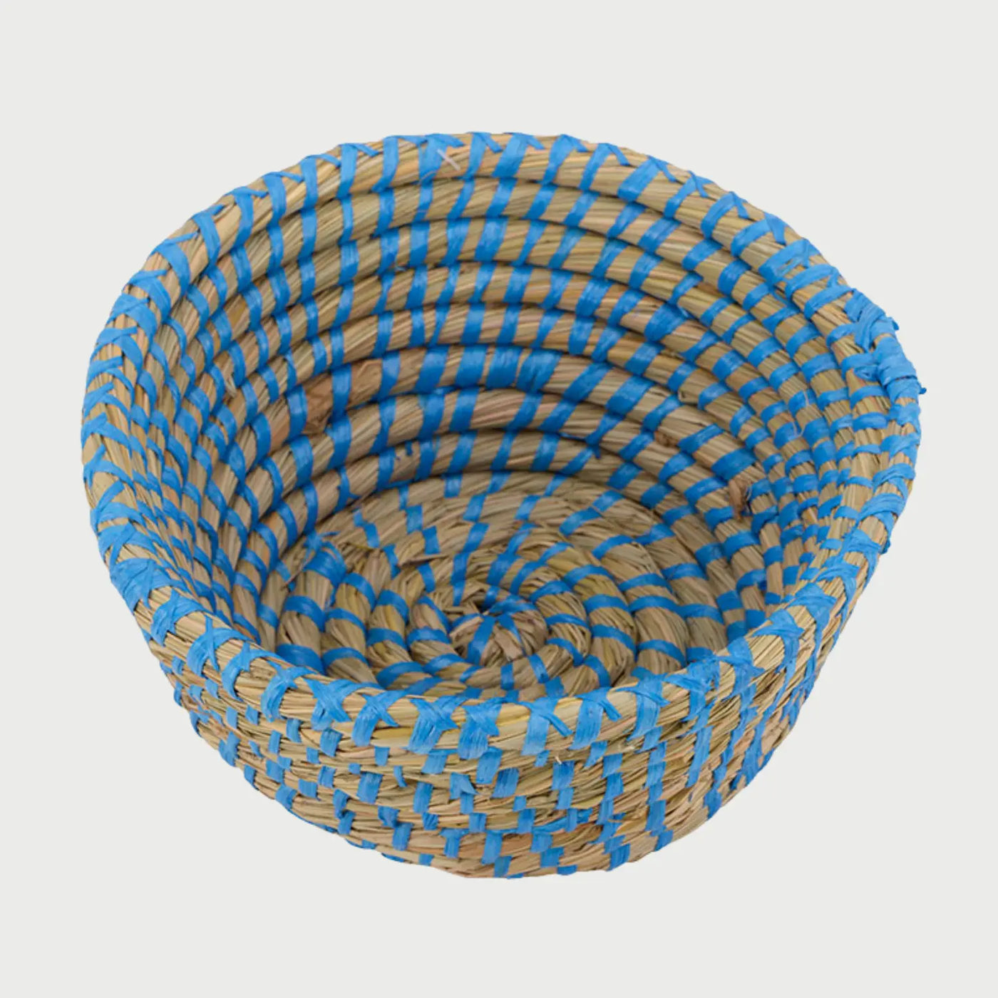 Vista de perfil de la canasta Damu azul; se aprecia la estructura cóncava y la repetición rítmica del hilo azul sobre la fibra natural, destacando un acabado artesanal y una textura táctil definida.