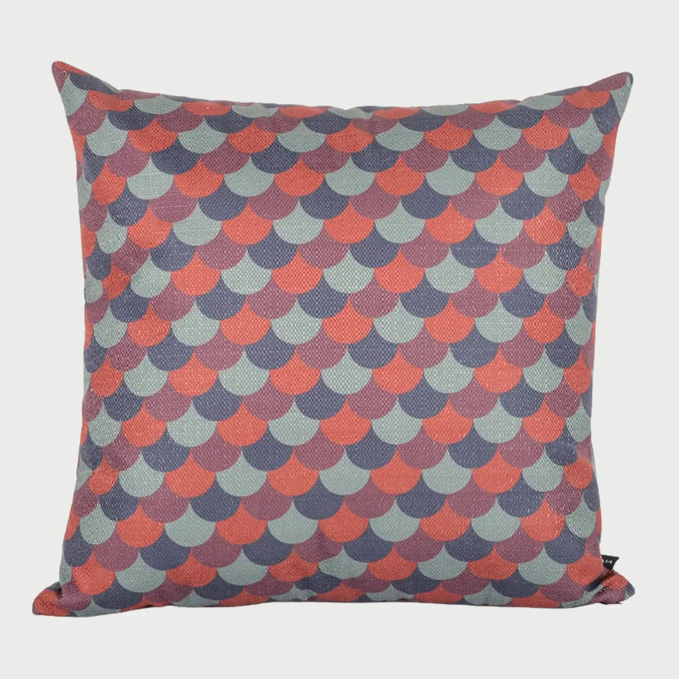 Vista frontal del cojín cuadrado Coto de 45 x 45 cm; presenta un patrón repetitivo de escamas o abanicos entrelazados en una paleta de colores terracota, azul petróleo y gris pizarra sobre un fondo de textura textil visible.