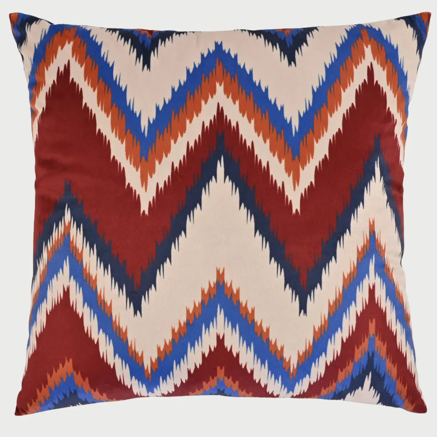 Vista frontal del cojín cuadrado Groovy de 50 x 50 cm; presenta un diseño dinámico de zigzag o "chevron" con bordes dentados que combinan franjas en color rojo quemado, azul vibrante, naranja y beige, evocando una estética retro de los años 70.