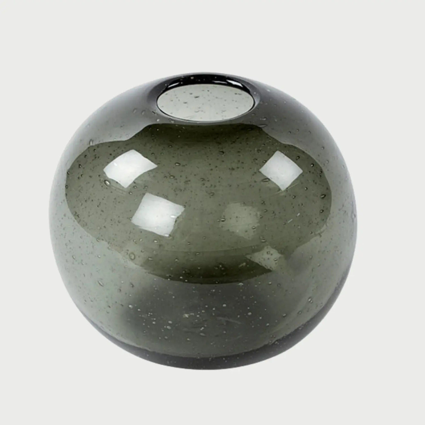 Vista frontal del florero Sirene de forma esférica; fabricado en vidrio soplado de color gris transparente, presenta una superficie lisa con sutiles burbujas internas que aportan una textura orgánica y artesanal.