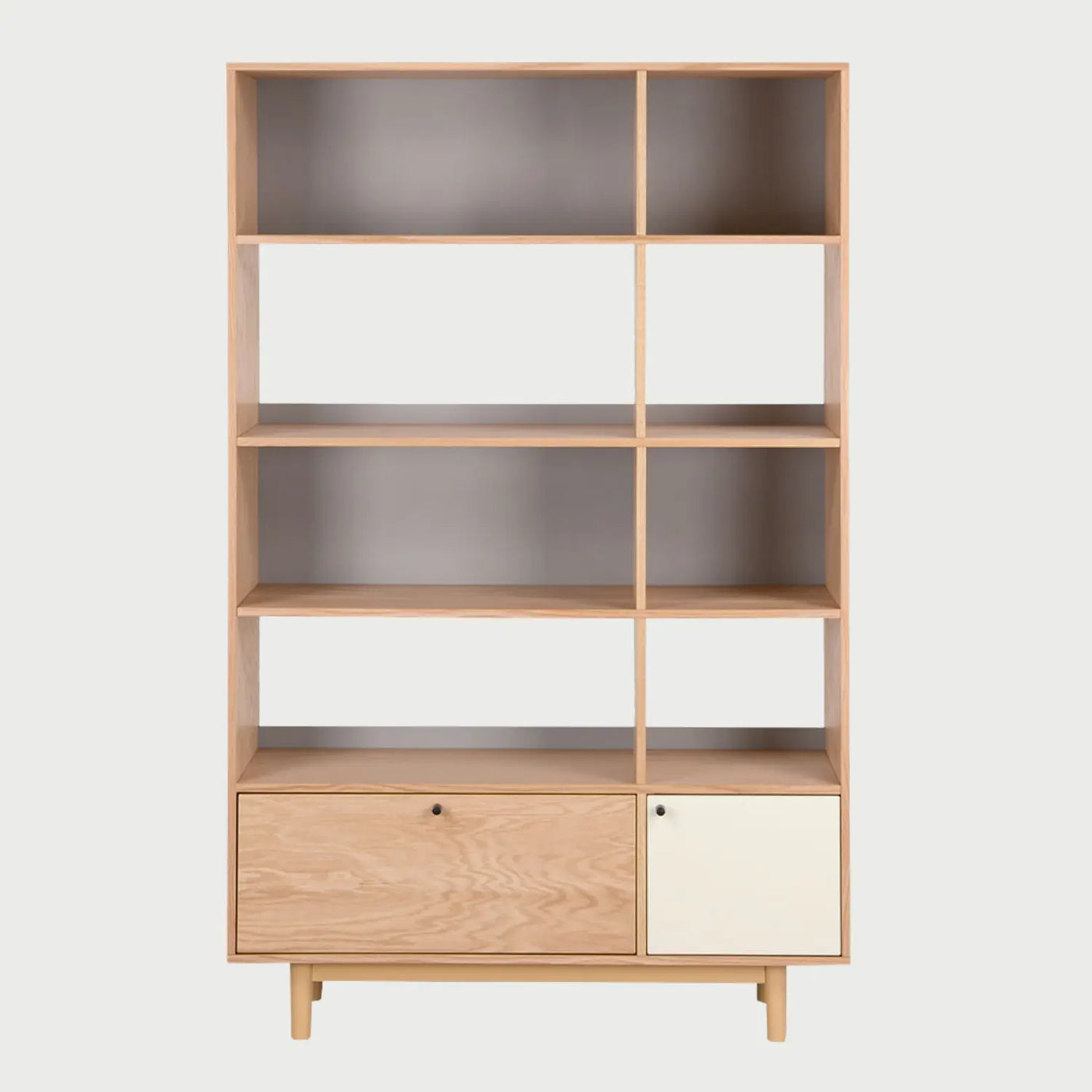 Vista frontal del librero Neo con estructura de madera en acabado encino, que cuenta con tres niveles de repisas abiertas asimétricas y una sección inferior con un cajón de madera y una puerta en color blanco mate.