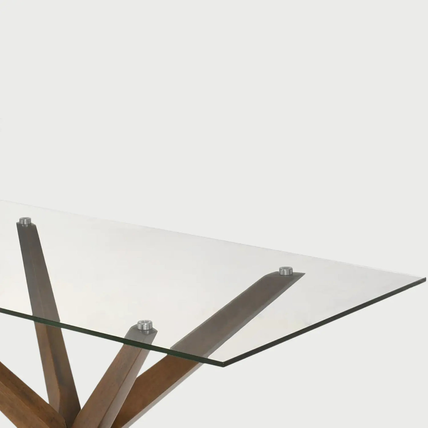 Detalle del herraje de acero que une la cubierta de cristal con la base de madera nogal; se aprecia el diseño dinámico de las patas angulares que convergen en un punto central, aportando un estilo escultórico y moderno.