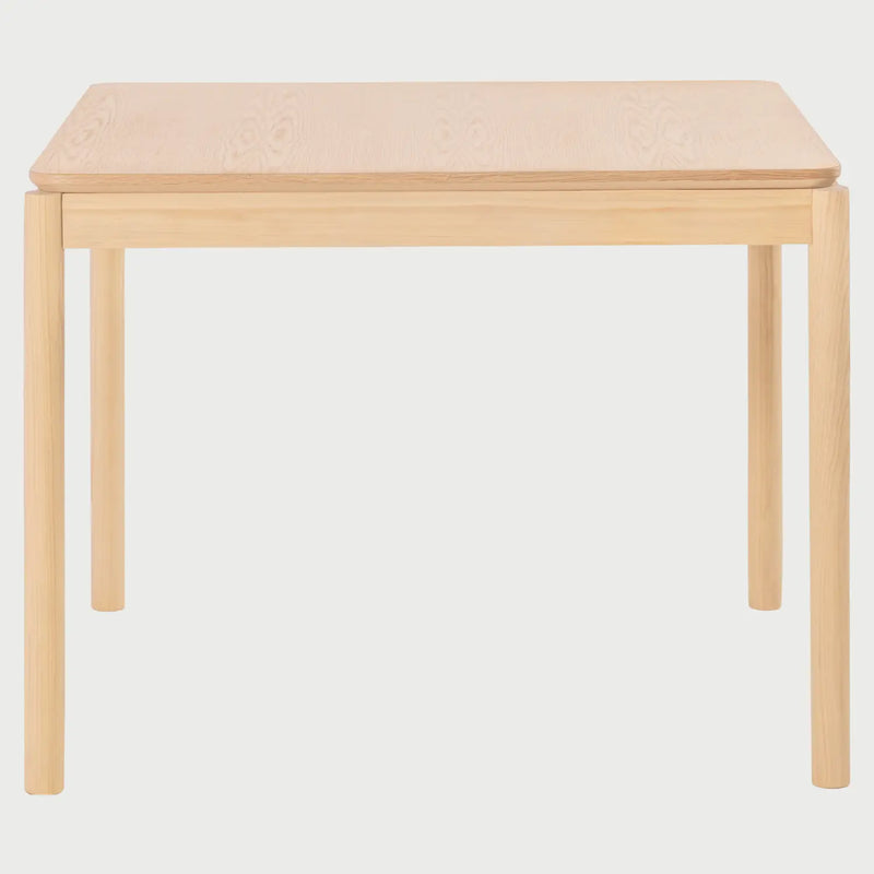 Vista frontal de la mesa de comedor cuadrada Akari de 100 cm; presenta una superficie plana de madera de encino en tono beige con esquinas suavemente redondeadas y cuatro patas cilíndricas robustas que brindan un soporte estable.