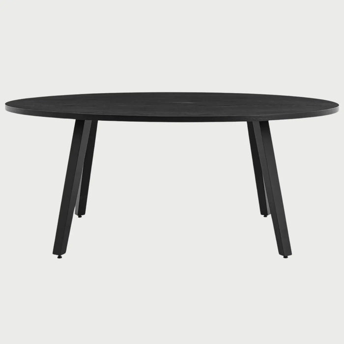 Vista frontal de la mesa de comedor ovalada Xocos en color negro; su acabado oscuro y monocromático enfatiza la silueta geométrica de las patas y la elegancia de la forma elíptica.