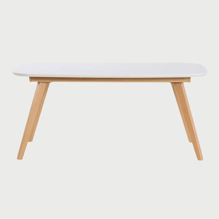 Vista frontal de la mesa de comedor Sei de 160 cm; presenta una superficie rectangular blanca con esquinas redondeadas y una base de cuatro patas angulares en madera clara de encino, combinando frescura y estabilidad.