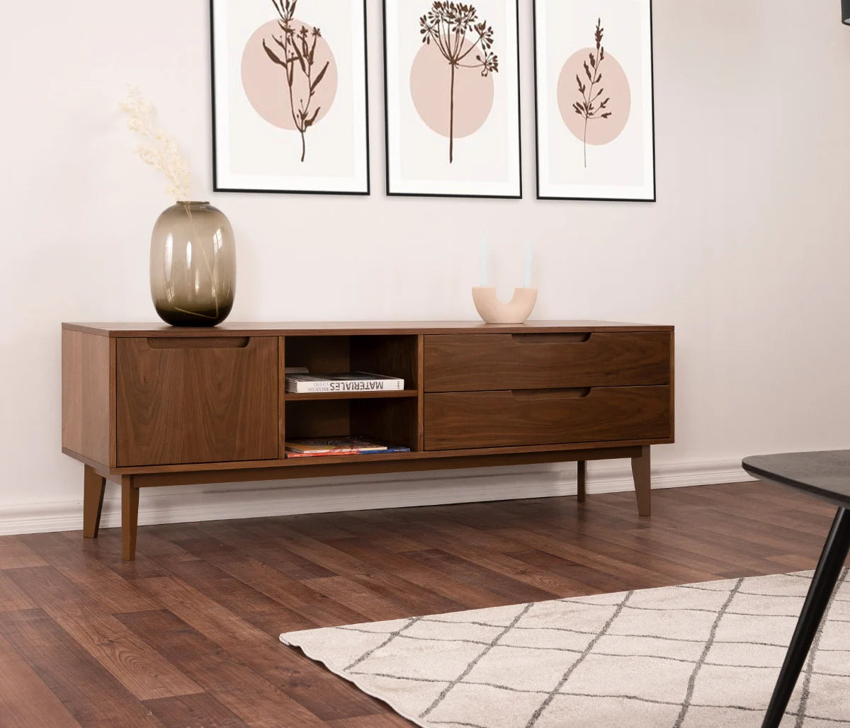 Mueble de TV Talitha de 160 cm en nogal ambientado en una sala de estar moderna. Destaca el contraste de la veta oscura de la madera contra paredes blancas y la organización asimétrica de sus compartimentos frontales