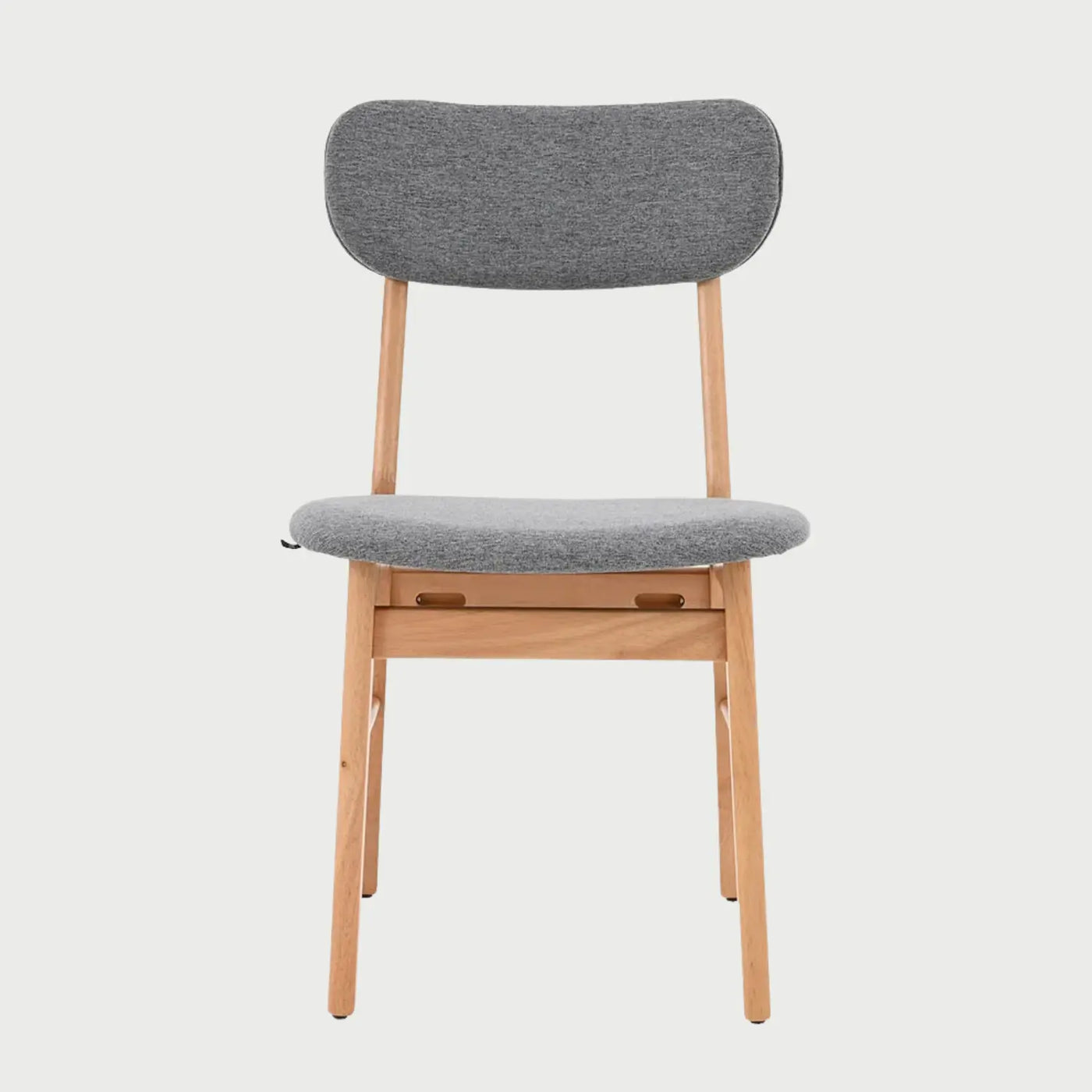 Vista frontal de la silla Marcela con estructura de madera en acabado encino natural y asiento acolchado tapizado en tela gris; destaca su respaldo ovalado horizontal y patas cilíndricas.