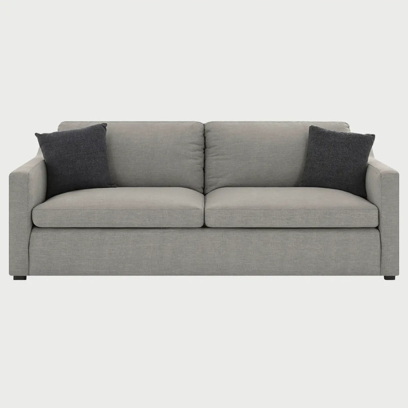 Vista frontal del sillón Marie de tres cuerpos en tela gris claro, destacando su silueta limpia y la organización proporcional de sus tres plazas con acentos textiles oscuros.