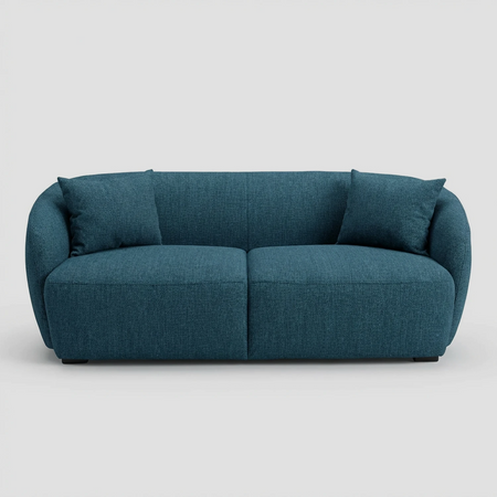 Vista frontal del sofá Kant GAIA de dos cuerpos en tela azul, destacando su diseño redondeado sin aristas, brazos integrados envolventes y dos cojines decorativos cuadrados a juego.