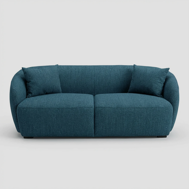 Vista frontal del sofá Kant GAIA de dos cuerpos en tela azul, destacando su diseño redondeado sin aristas, brazos integrados envolventes y dos cojines decorativos cuadrados a juego.