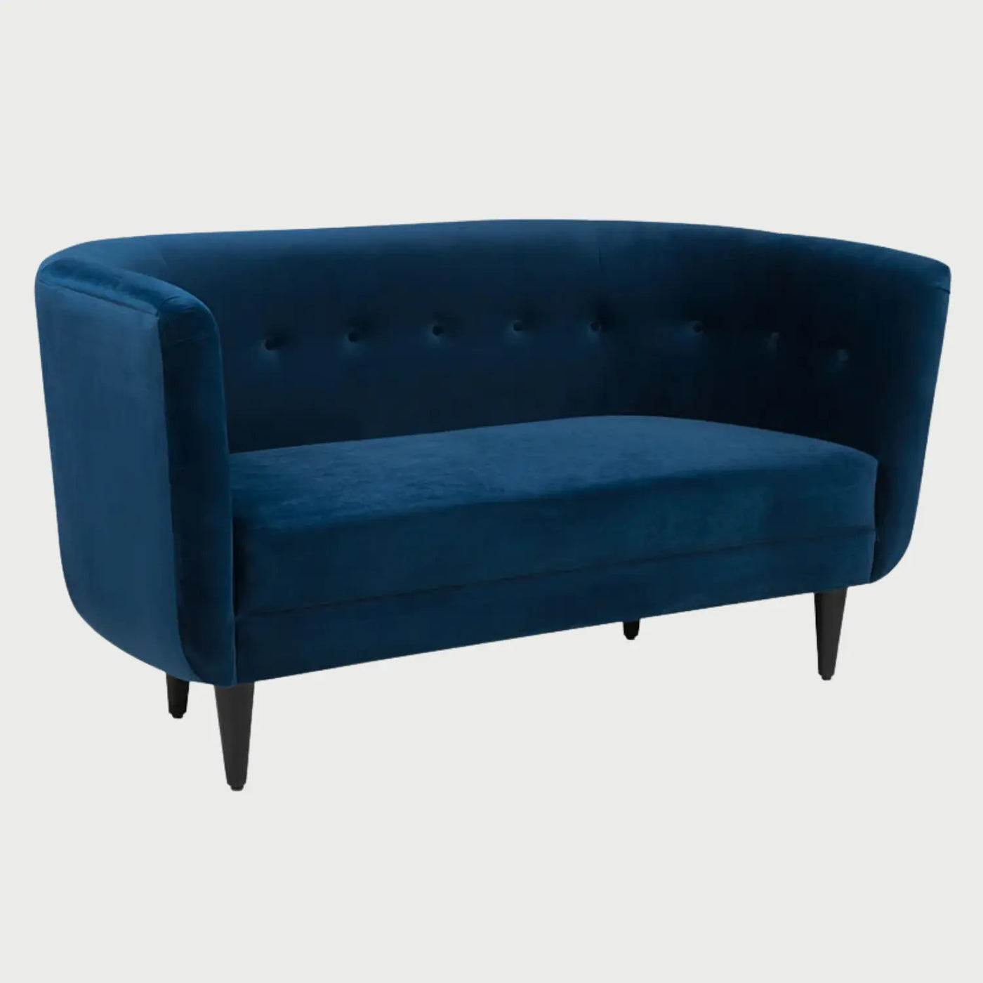 Vista lateral del sofá Tavari azul, resaltando la silueta envolvente del respaldo "tub-style" y la ligera inclinación de las patas traseras que le otorgan estabilidad y un aire retro.