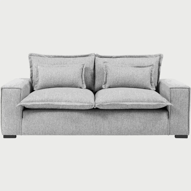Vista frontal del sofá Emilia GAIA de tres cuerpos en tela color gris, destacando sus asientos de gran formato, cojines de respaldo dobles superpuestos y brazos rectos que acentúan su diseño moderno y acogedor.