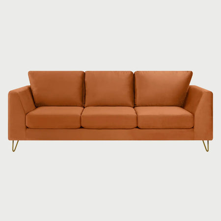 Vista frontal del sofá Yoco de tres cuerpos en terciopelo naranja, con tres cojines de respaldo y tres de asiento, resaltando el brillo del tejido y patas metálicas tipo horquilla en color dorado.