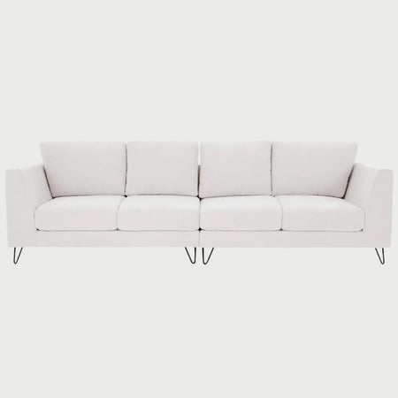 Vista frontal del sofá Yoco de cuatro plazas tapizado en tela blanca, compuesto por cuatro cojines de respaldo y cuatro de asiento simétricos, elevado sobre patas de madera en acabado nogal que aportan un contraste elegante y natural.