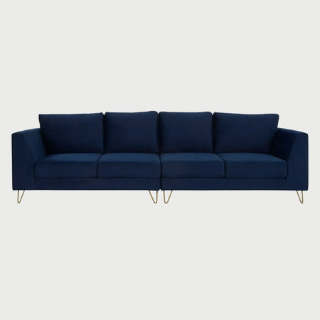 Vista frontal del sofá Yoco de cuatro plazas tapizado en terciopelo azul marino, con cuatro cojines de respaldo y asiento individuales, elevado sobre elegantes patas metálicas tipo horquilla en acabado dorado.