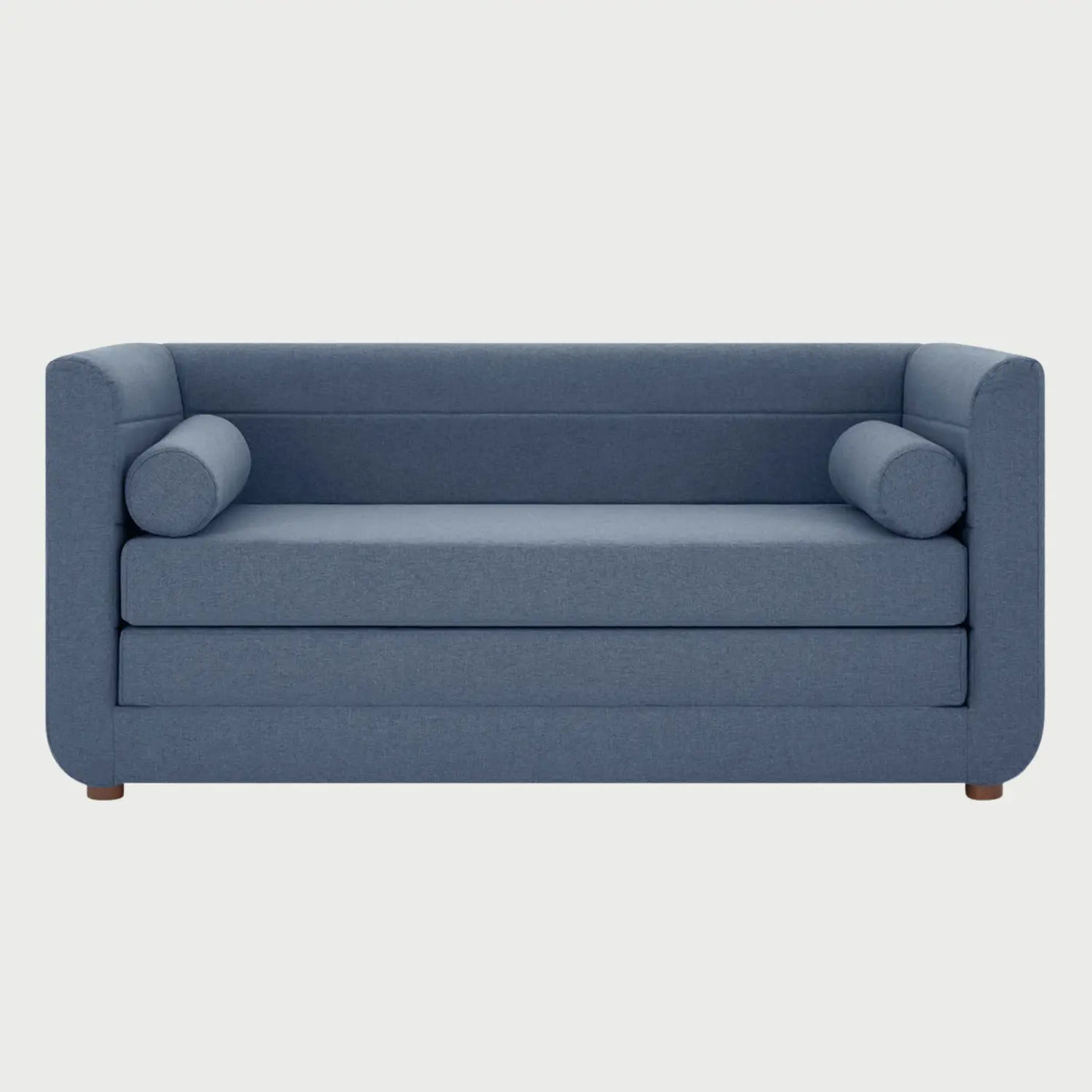 Vista frontal del sofá cama Basil en tela azul, con diseño de respaldo bajo, dos cojines cilíndricos laterales y patas de madera en acabado nogal oscuro.