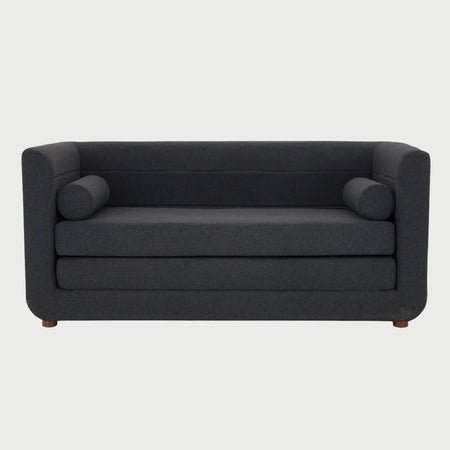 Vista frontal del sofá cama Basil en color gris oscuro, destacando la sobriedad del textil en combinación con las patas de madera en acabado nogal.