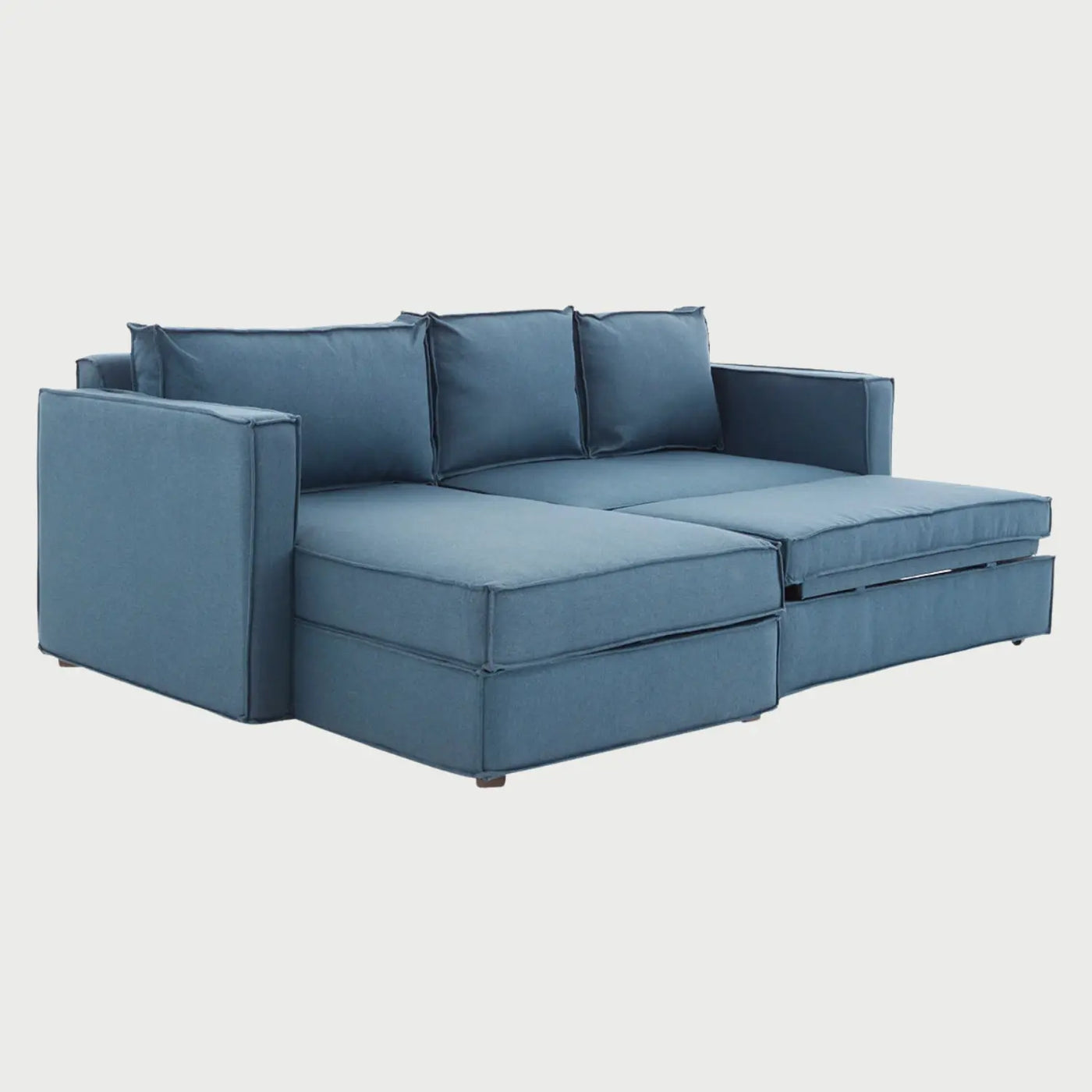 Vista lateral del sofá cama Yamanik azul, mostrando la extensión del chaise longue y el perfil robusto de los descansabrazos que enmarcan la estructura modular.