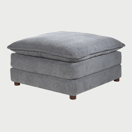 Vista frontal del taburete Andrea tapizado en tela gris jaspeada, destacando su cojín superior de gran volumen y suavidad sobre una base cuadrada acolchada con patas de madera cortas.