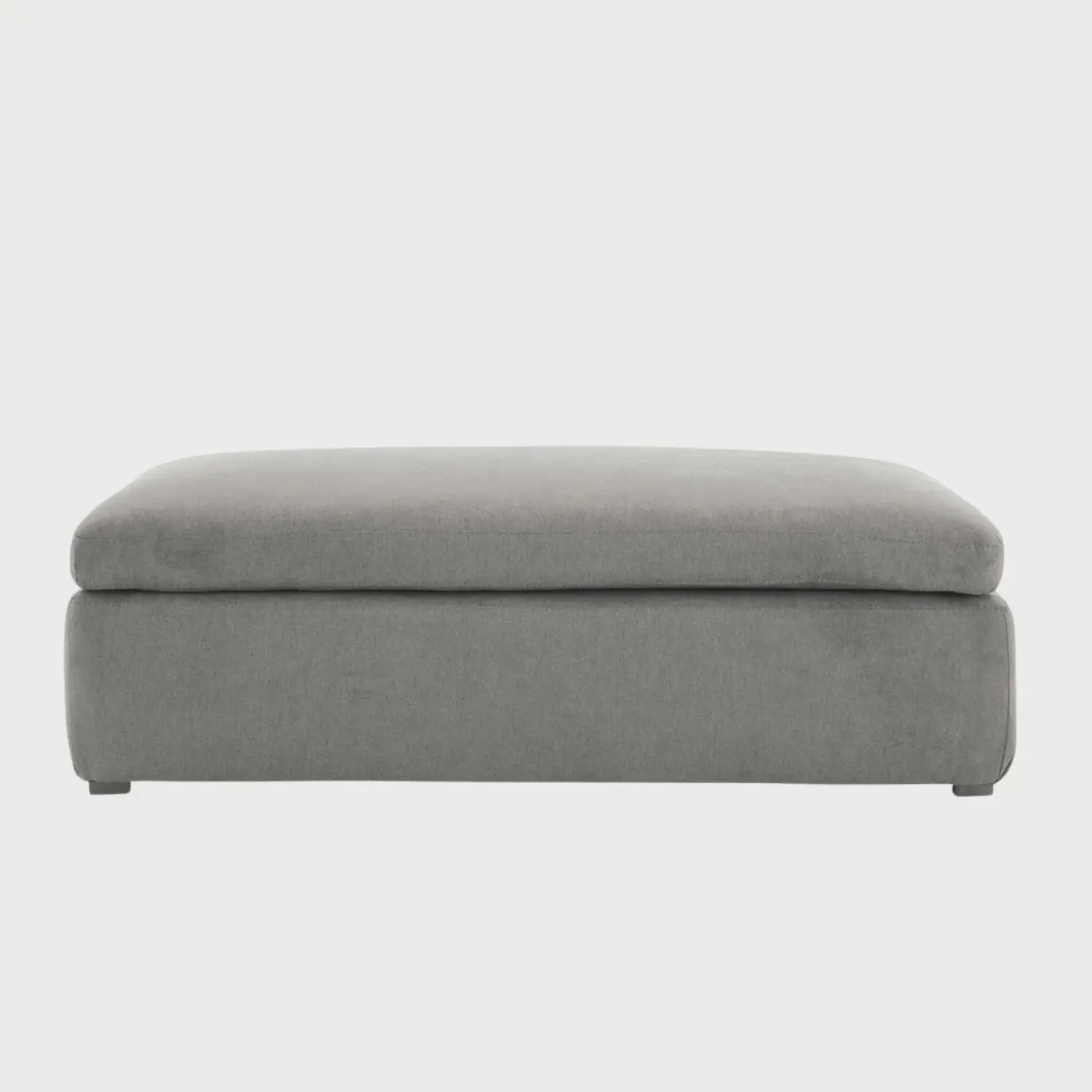 Vista frontal del taburete Marie en color gris, con un diseño rectangular alargado, cojín superior de gran espesor y base tapizada liza que llega casi al nivel del suelo.