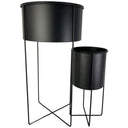 Juego de 2 maceteros Ureña en color negro, con soportes metálicos de diferentes alturas y forma cilíndrica.