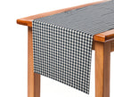 Camino de mesa con diseño de cuadros chicos en blanco y negro, elegantemente drapeado sobre una mesa de madera.