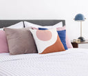 Cojín Ocaso de 50 x 50 cm con un diseño circular en tonos rosa, azul y marrón, ideal para decorar tu habitación con estilo.