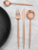 Juego de cubiertos en color bronce de GAIA, que incluye cuchara, tenedor, cuchillo y cuchara de postre sobre una superficie de mármol.
