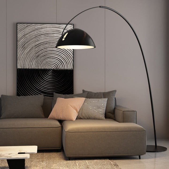 Lámpara de piso Pluma con brazo curvado y pantalla redonda, situada junto a un sofá moderno en un ambiente contemporáneo.