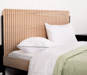 Imagen de ambientación que muestra un set de almohadas Premium blancas sobre una cama con sábanas claras y un edredón verde oliva, resaltando su diseño elegante frente a una cabecera de madera estriada.
