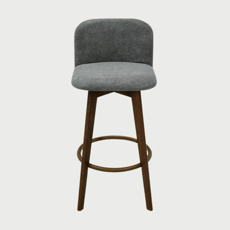 Vista frontal del banco alto Leco tapizado en tela gris con textura, con un respaldo bajo redondeado, asiento acolchado y patas de madera en acabado nogal con un reposapiés circular metálico.