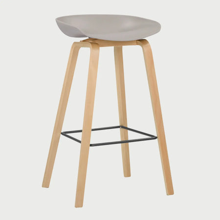 Vista lateral del banco alto Perique beige, mostrando la curvatura del asiento y la inclinación de sus patas de madera que proporcionan una base estable y un estilo de inspiración nórdica.