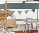 Imagen de ambientación de los banderines Niove en tonos verdes decorando la parte inferior de una cama litera; el espacio incluye una mesa de actividades gris y un baúl de madera, creando una atmósfera lúdica y organizada.