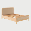 Acercamiento al acabado de la cama Iki, donde se aprecia la veta natural de la madera clara y la suavidad del tapizado beige integrado en los marcos curvos, resaltando su diseño de estilo Japandi.