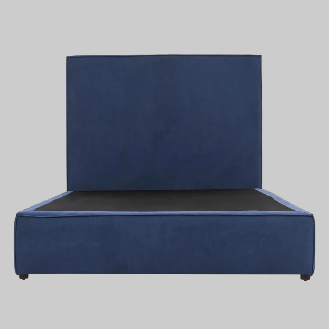 Vista frontal de la cama matrimonial Raquel; presenta una imponente cabecera alta y rectangular tapizada en terciopelo azul profundo que se integra con una base de perfil bajo del mismo tono, creando una silueta moderna y sofisticada.