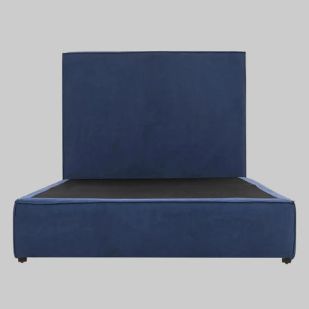 Vista frontal de la cama matrimonial Raquel; presenta una imponente cabecera alta y rectangular tapizada en terciopelo azul profundo que se integra con una base de perfil bajo del mismo tono, creando una silueta moderna y sofisticada.