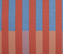 Acercamiento al textil del cojín Enea; muestra la trama cerrada de la tela y la transición limpia entre los bloques de color azul y naranja, incluyendo la etiqueta lateral negra de GAIA en la esquina inferior.