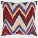 Vista frontal del cojín cuadrado Groovy de 50 x 50 cm; presenta un diseño dinámico de zigzag o "chevron" con bordes dentados que combinan franjas en color rojo quemado, azul vibrante, naranja y beige, evocando una estética retro de los años 70.