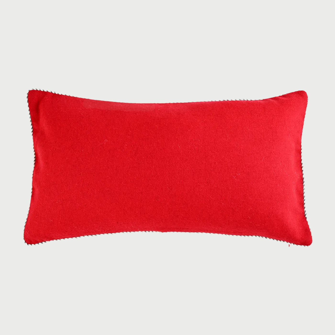 Vista frontal del cojín rectangular Víspera de 30 x 50 cm; fabricado en lana de color rojo intenso, destaca por su superficie lisa y un ribete decorativo bicolor en blanco y negro que recorre todo su perímetro.
