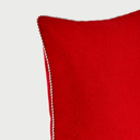Acercamiento al cojín Víspera cuadrado; se aprecia la trama densa y suave de la lana en color rojo intenso, junto con el detalle del ribete perimetral trenzado en hilos blanco y negro que define el borde con precisión.