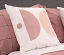 Cojín cuadrado Balance de 45x45 cm con diseño geométrico en tonos rosa y blanco, decorando una cama con ropa de cama a juego.