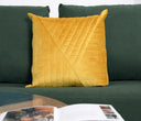 Cojín Bunek de 50x50 cm en dorado, con un diseño texturizado, colocado sobre un sofá verde junto a un libro abierto.